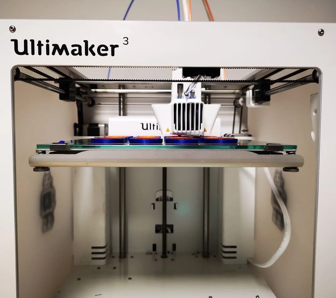 Impresora Ultimaker 3 produciendo una serie de piezas en azul y naranja
